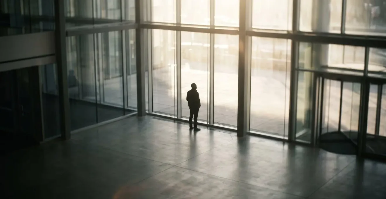 Silhouette humaine en contre-jour dans un hall vitré avec éclairage naturel intense
