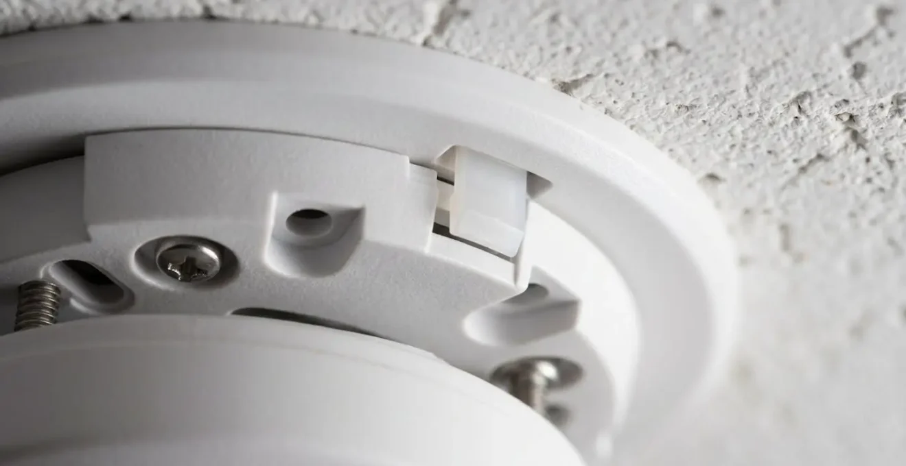 Gros plan technique d'un détecteur de fumée blanc au plafond avec sa platine de fixation et détails de montage