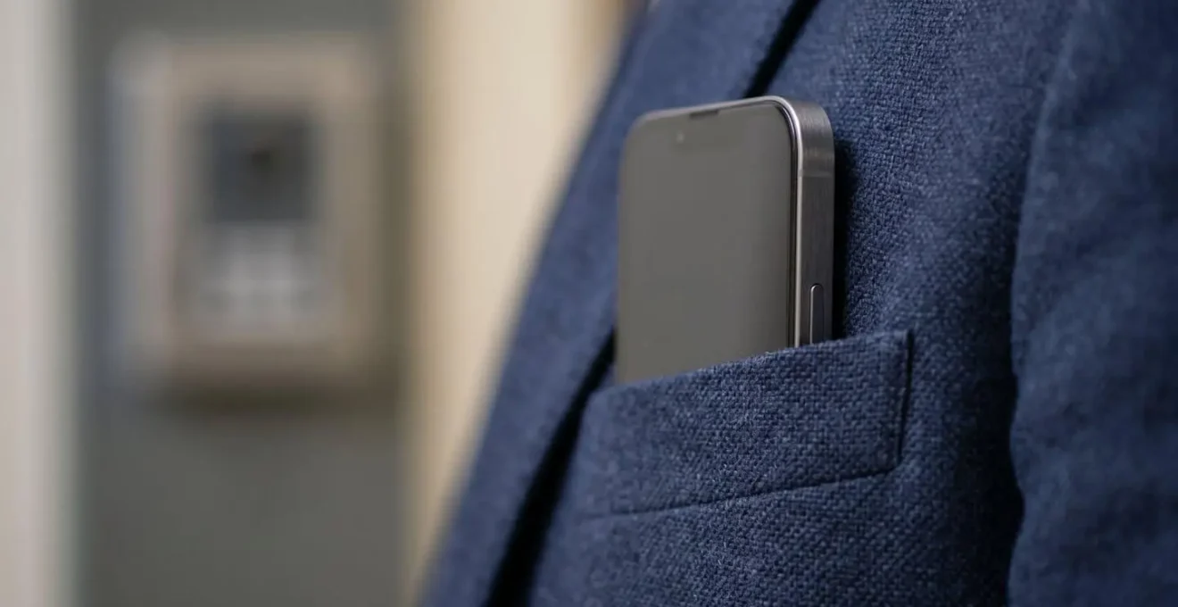 Gros plan macro sur la poche d'une veste de travail contenant un smartphone, avec en arrière-plan flou un lecteur de contrôle d'accès